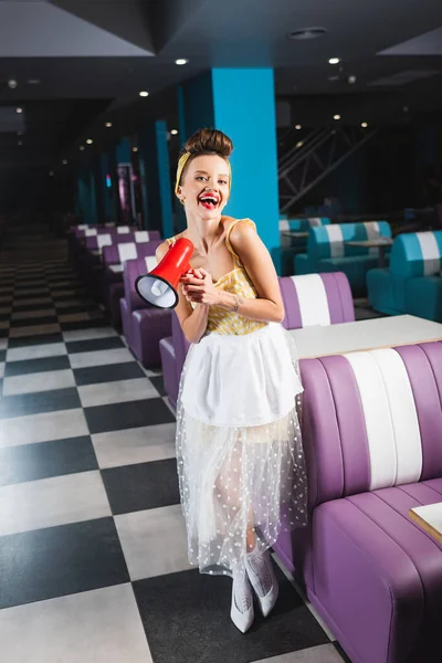 Happy young pin up woman holding megaphone in retro cafe — Stock Photo