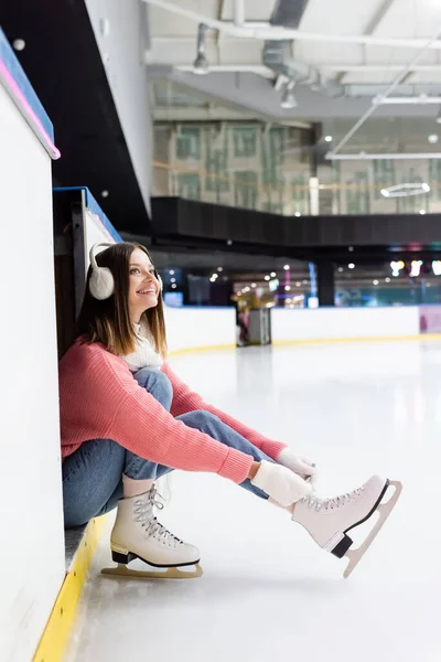 Alegre joven mujer atando cordones de zapatos en patines de hielo - foto de stock