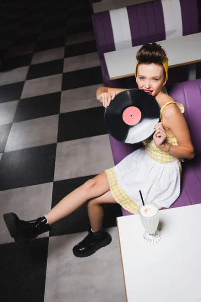 Vista de ángulo alto de la mujer joven pin up morder disco de vinilo retro - foto de stock