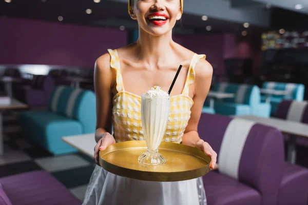 Cropped view of cheerful pin up waitress holding tray with milkshake in cafe — Stock Photo