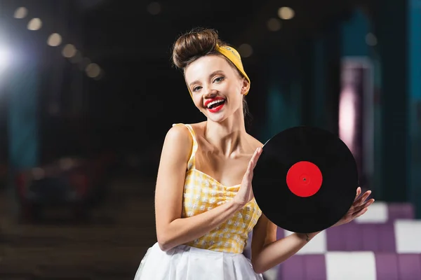 Complacido joven pin up mujer con labios rojos celebración de disco de vinilo retro - foto de stock