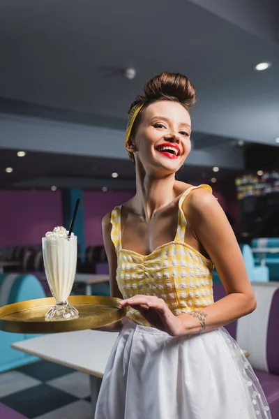 Gioiosa cameriera pin up con vassoio per tatuaggi e gustoso milkshake nel caffè — Foto stock