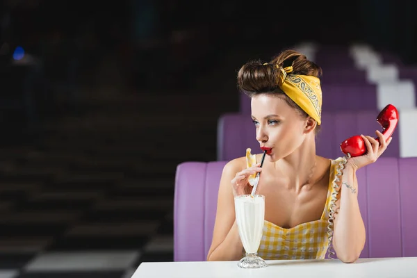 Молодая женщина держит ретро телефон и пьет молочный коктейль в кафе — стоковое фото