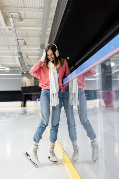 In voller Länge steht eine glückliche junge Frau im Winteroutfit auf der Eisbahn — Stockfoto