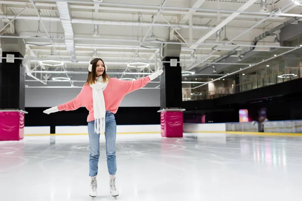 Piena lunghezza di felice giovane donna in inverno vestito pattinaggio con le mani tese sulla pista di pattinaggio su ghiaccio — Foto stock