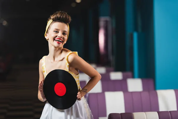 Женщина с красными губами, держащая в руках ретро-виниловый диск и улыбающаяся в кафе — стоковое фото