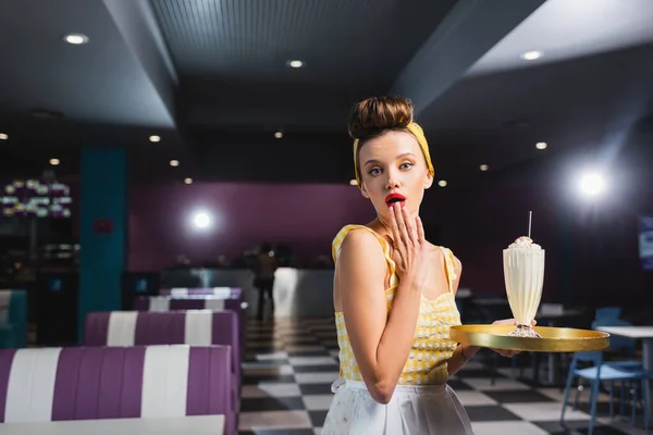 Chocado pin up camarera celebración bandeja con batido en la cafetería - foto de stock