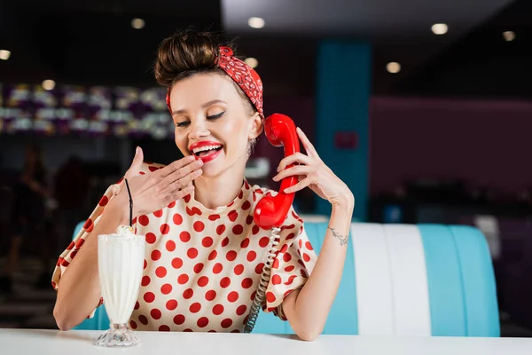 Felice pin up donna in camicia a pois parlando sul telefono retrò vicino milkshake sul tavolo — Foto stock