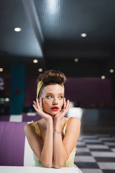 Giovane pin up donna con tatuaggio guardando lontano nel caffè — Foto stock