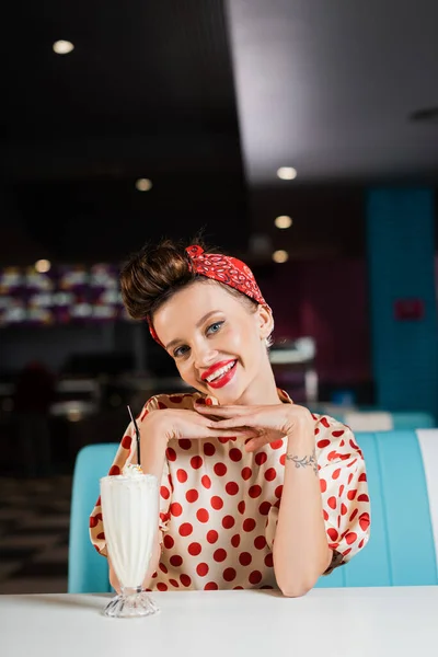 Alegre pin up mujer con labios rojos y lunares blusa cerca de batido - foto de stock