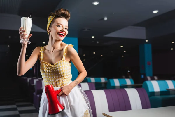 Happy pin up woman with megaphone and milkshake in cafe — Stock Photo