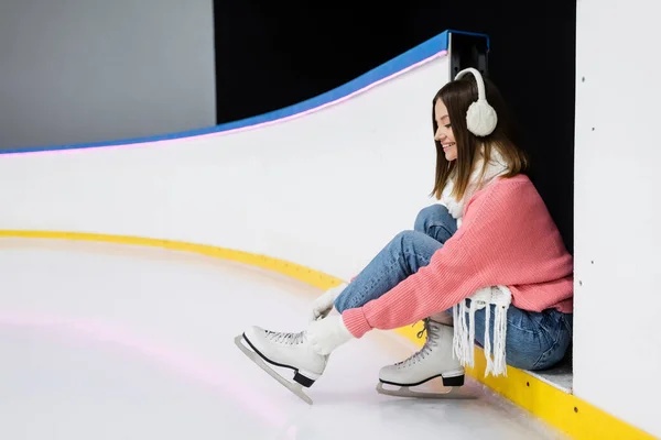 Cheerful young woman in winter outfit tying shoe laces on ice skates — Stock Photo