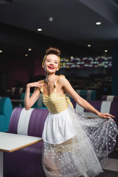 Alegre pin up camarera en vestido sonriendo en la cafetería - foto de stock