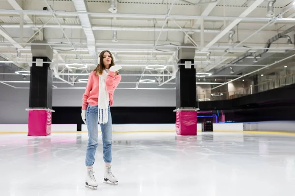 Longitud completa de la joven feliz en traje de invierno patinaje y envío de beso de aire en pista de hielo - foto de stock