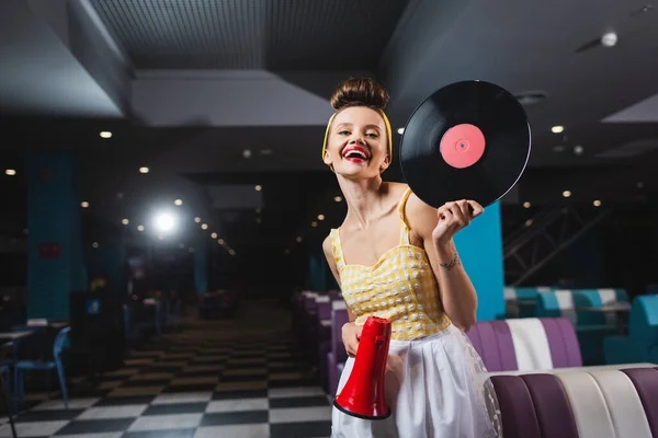 Happy pin up woman with megaphone and vinyl disc in cafe — Stock Photo
