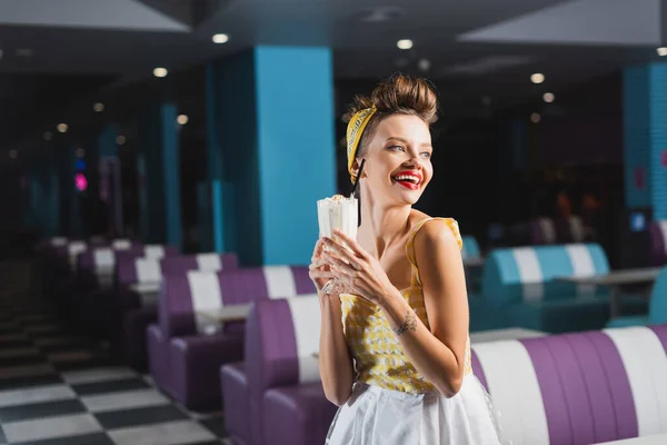 Весёлая женщина в платье держит вкусный молочный коктейль в кафе — стоковое фото