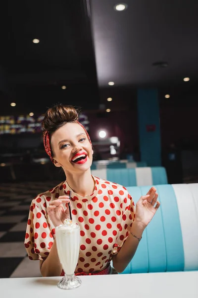 Позитивна жінка в червоній блузці з крапкою полка біля молочного коктейлю на столі — стокове фото