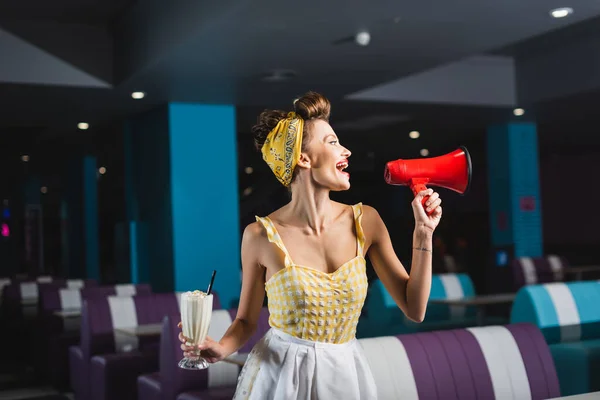 Fröhliche Kellnerin hält Milchshake in der Hand und schreit in Megafon — Stockfoto