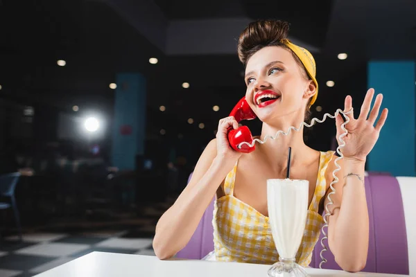 Щаслива піна жінка говорить на ретро телефоні біля молочного коктейлю на столі в кафе — стокове фото