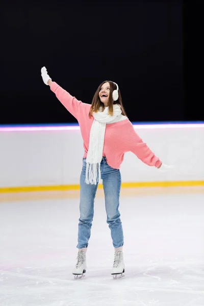 Comprimento total da mulher feliz no ouvido muffs e inverno roupa patinação na pista de gelo — Fotografia de Stock