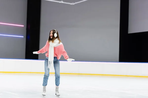 Pleine longueur de femme heureuse en cache-oreilles et tenue d'hiver patinant sur patinoire gelée — Photo de stock