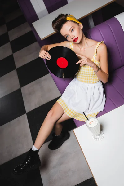 Vista de ángulo alto de la mujer pin up con los labios rojos que sostienen el disco de vinilo en la cafetería - foto de stock