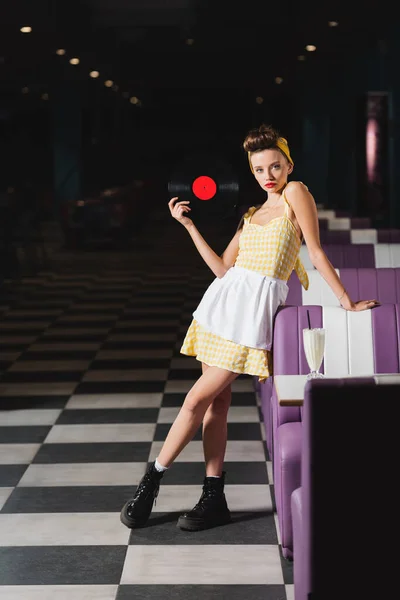 Comprimento total de jovem pin up mulher com lábios vermelhos segurando disco de vinil no café — Fotografia de Stock