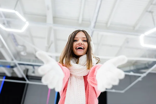 Low angle view of cheerful young woman in ear muffs and scarf gesturing while looking at camera — Stock Photo