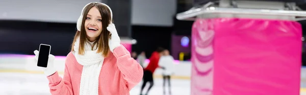 Happy woman in ear muffs holding smartphone with blank screen, banner — Stock Photo