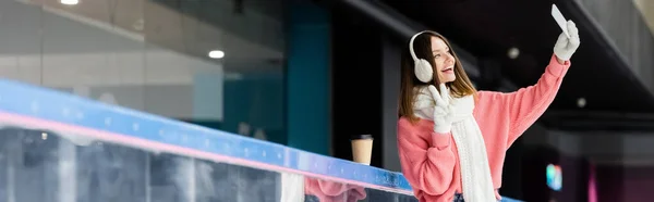 Happy woman in ear muffs showing peace sign and taking selfie, banner — Stock Photo