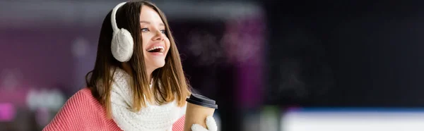 Mujer feliz en orejeras y bufanda sosteniendo taza de papel, bandera - foto de stock