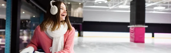 Mujer joven excitada en orejeras y bufanda riendo en pista de hielo, pancarta - foto de stock