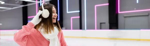 Pleased woman in pink sweater adjusting white ear muffs, banner — Stock Photo