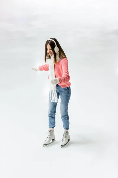 Повна довжина позитиву молода жінка катається на ковзанах з витягнутими руками на замерзлій ковзанці — стокове фото