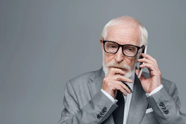 Pensativo hombre de negocios de edad hablando en el teléfono móvil aislado en gris - foto de stock