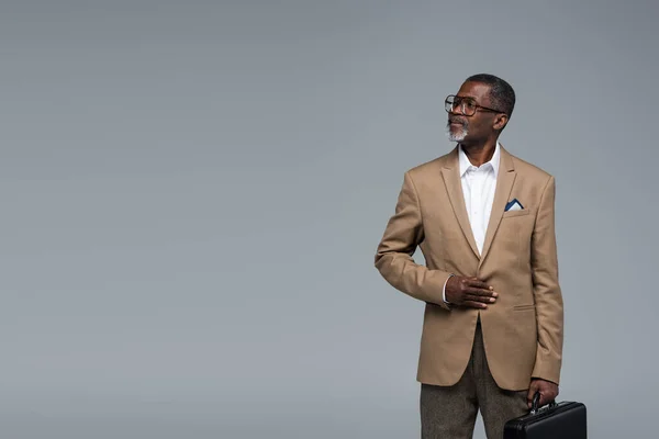 Senior and confident african american businessman with briefcase looking away isolated on grey — Stock Photo