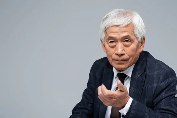 Senior asian businessman with outstretched hand looking at camera isolated on grey — Stock Photo