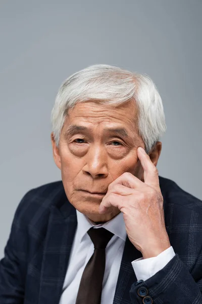 Portrait of senior asian businessman with hand near face looking at camera isolated on grey — Stock Photo