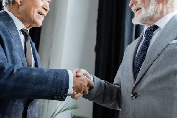 Частичный взгляд старших успешных бизнесменов, пожимающих руки в офисе — стоковое фото