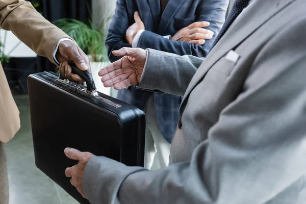 Teilansicht eines afrikanisch-amerikanischen Mannes, der Geschäftspartner im Büro eine Aktentasche schenkt — Stockfoto