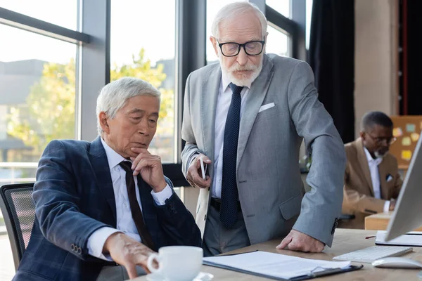 Socios comerciales interraciales senior que buscan un contrato mientras trabajan en la oficina - foto de stock