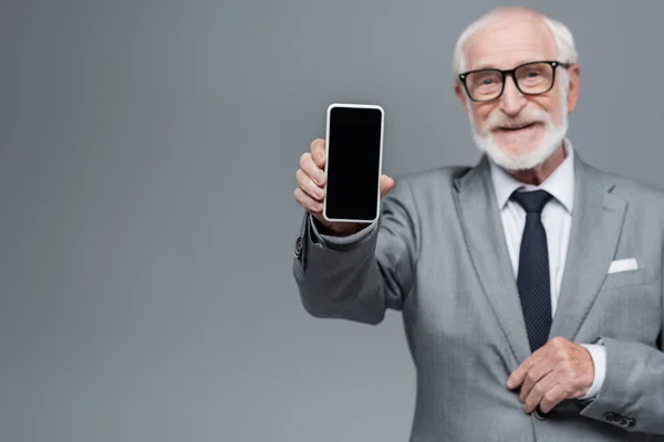 Unscharfer Senior-Geschäftsmann zeigt Handy mit leerem Bildschirm isoliert auf grau — Stockfoto