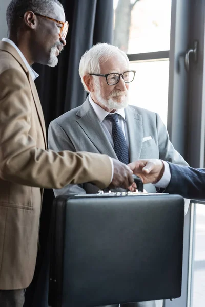 Senior interracial businessmen giving briefcase to business partner in office — Stock Photo