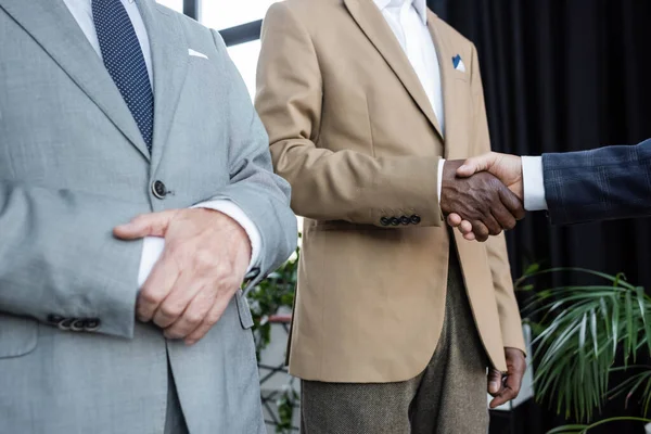 Vue recadrée des principaux partenaires d'affaires multiethniques serrant la main au bureau — Photo de stock