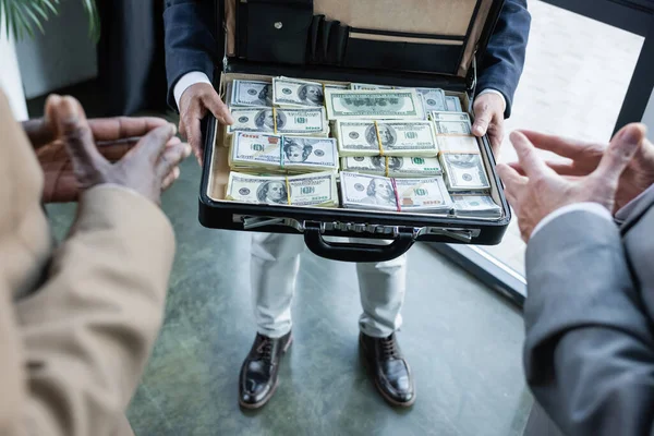 Visão parcial de parceiros de negócios desfocados perto do homem com dólares em pasta — Fotografia de Stock