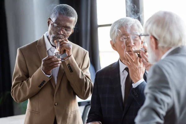 Successful senior multiethnic business partners smoking cigars in office — Stock Photo