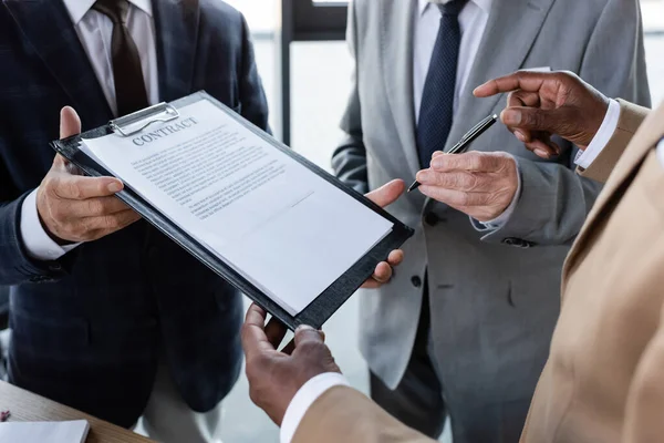 Vista recortada de empresarios senior que dan contrato y pluma a socio de negocios afroamericano - foto de stock