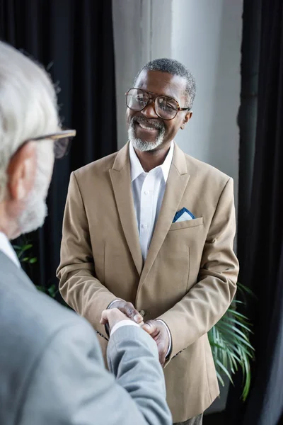 Empresário americano africano feliz apertando as mãos com parceiro de negócios sênior em primeiro plano turvo — Fotografia de Stock