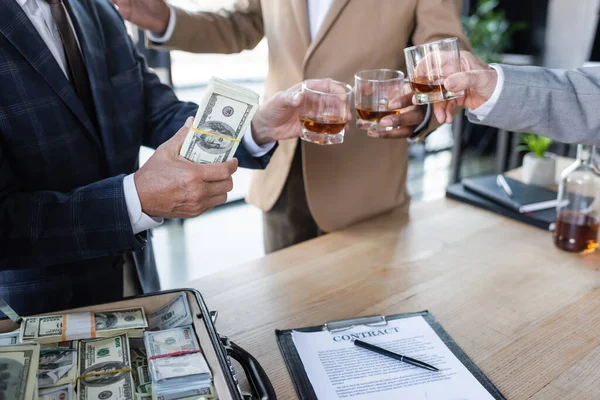 Vista cortada de empresário segurando dólares enquanto clinking óculos perto de contrato e pasta — Fotografia de Stock