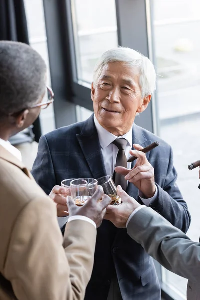 Senior asiatique homme d'affaires souriant tout en cliquetis verres de whisky avec des partenaires d'affaires — Photo de stock